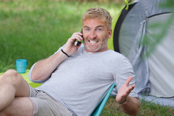 man camping teeth gritted while talking on telephone - Фото, изображение