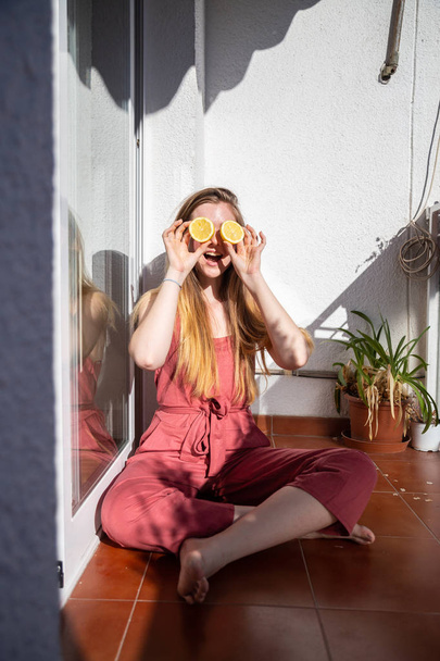Nuori onnellinen kaunis nainen rento kesämekko istuu terassilla ja peittää silmät kypsä sitruunat
 - Valokuva, kuva