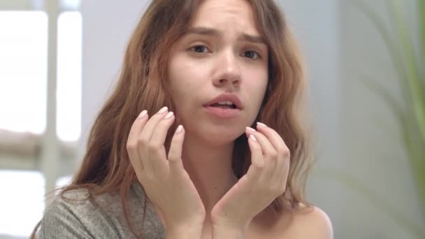 Ontevreden vrouw die de gezichtshuid aanraakt in de badkamerspiegel. Probleemhuidconcept - Video