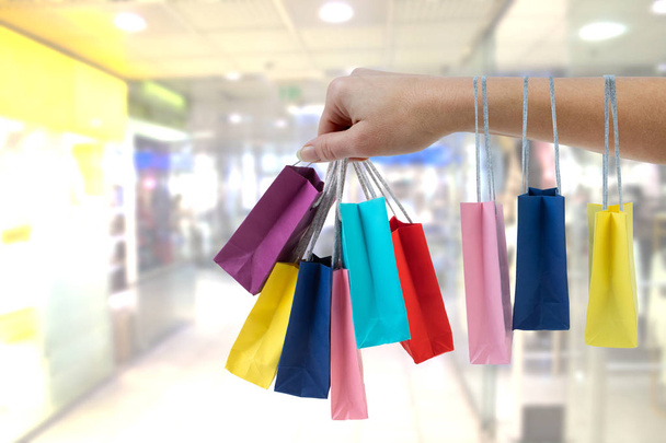 Crop female hand holding colorful paper bags on background of shopping center. - Photo, Image