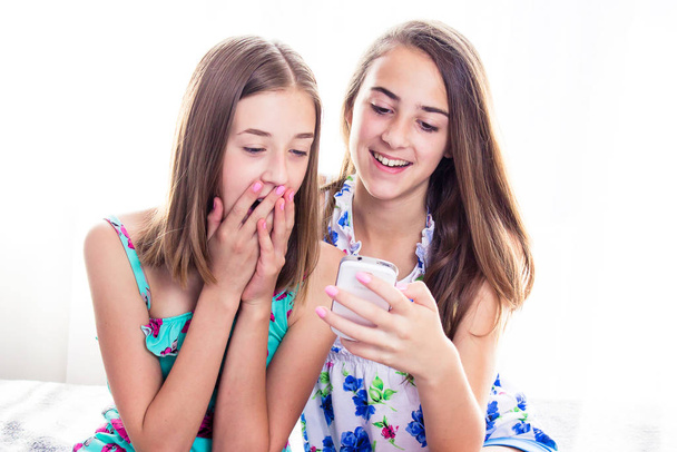 Two girls in colorful summer dresses looking at smart phone - Fotoğraf, Görsel