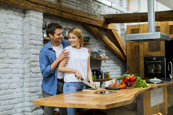 Lovely cheerful young couple cooking dinner together and having fun at rustic kitchen - 写真・画像