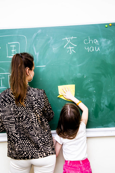 girl and teacher wipes a green school board from Chinese characters - 写真・画像