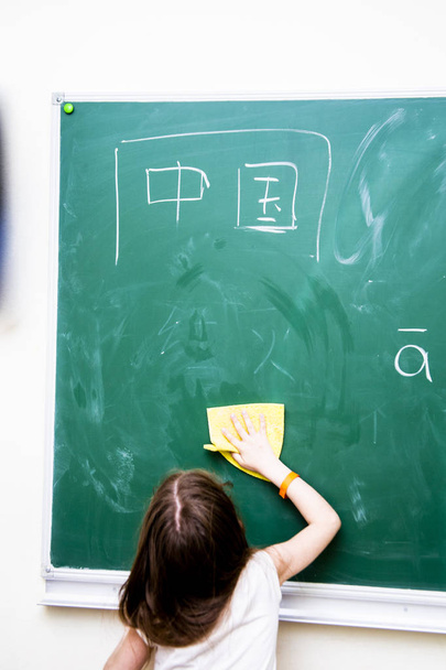 girl wipes a green school board from Chinese characters - Valokuva, kuva