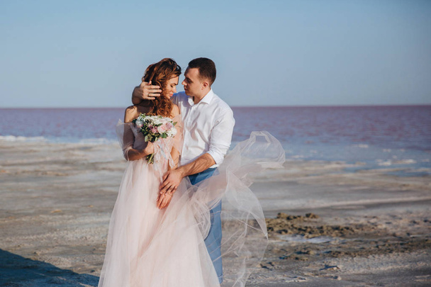 beautiful newlyweds on the sea shore and gentle groom, touching the brides hair. front view. - Foto, immagini