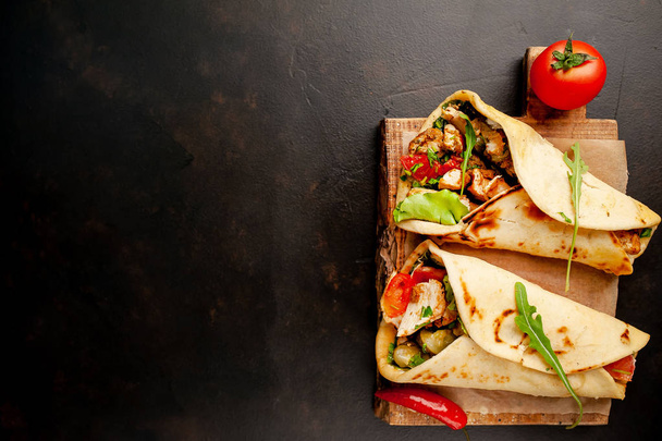 Tacos mexicanos tradicionais com salada em tábua de cortar madeira sobre fundo de concreto preto
 - Foto, Imagem