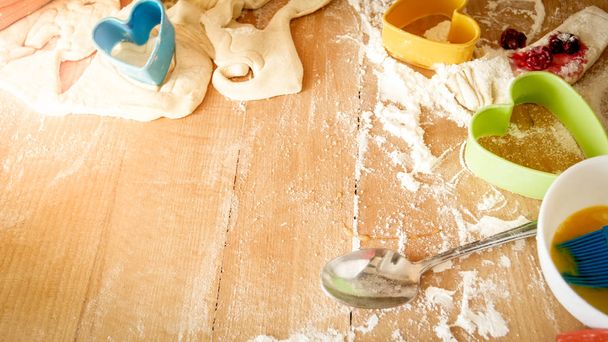 Close-up foto van vers deeg, eieren, melk, en veel gereedschappen voor bakkerij en koken liggend op de grote houten keuken tegen bord - Foto, afbeelding
