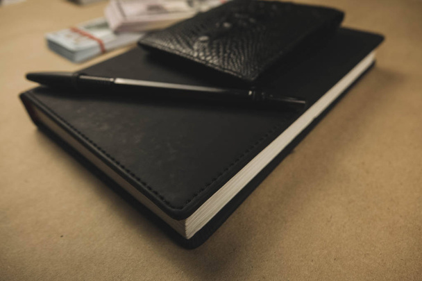 Černý zápisník, pero a dolarové hotovostní bankovky na dřevěné pozadí-koncepce finančního řízení nebo plánování, vydělání peněz z externě psaného zápisu - Fotografie, Obrázek