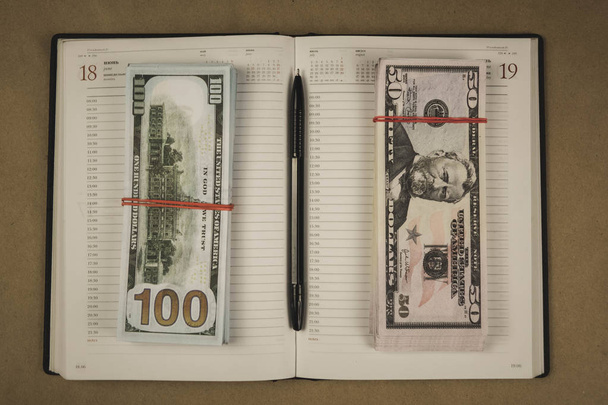 A pack of dollars and a notebook open with a pencil on a wooden background - Photo, Image