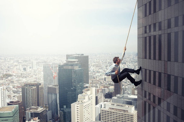 Ο επιχειρηματίας σκαρφαλώνει σε ένα κτίριο με σχοινί. Έννοια προσδιορισμού - Φωτογραφία, εικόνα