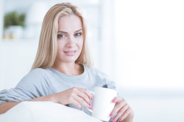 Portrait of a young woman sitting on sofa with cup of coffee - Fotografie, Obrázek