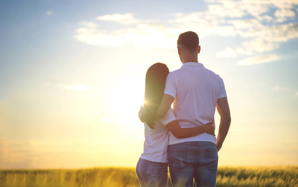愛情深い若いカップルのバックビューは、密接に立って、自然を賞賛し、距離に何かを見て、夕日を楽しむ、脇にコピースペース - 写真・画像