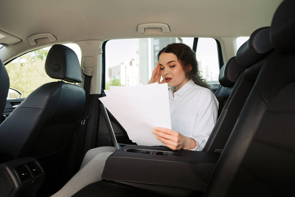Upset confused business woman reading bad-news message, working with documents and laptop in a car. - Foto, Imagem
