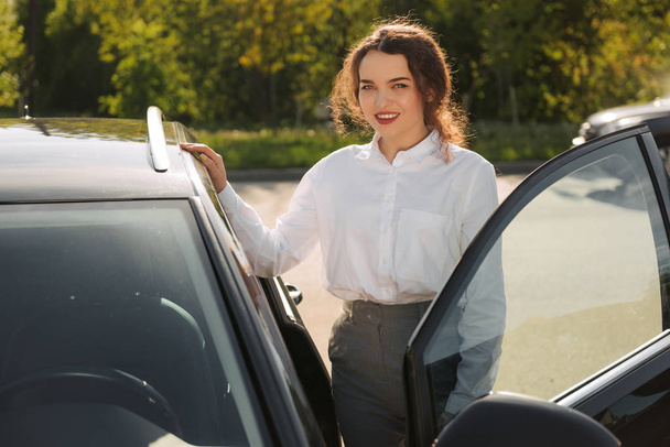 Business woman standing near her car with sunny weather outdoors. - Zdjęcie, obraz