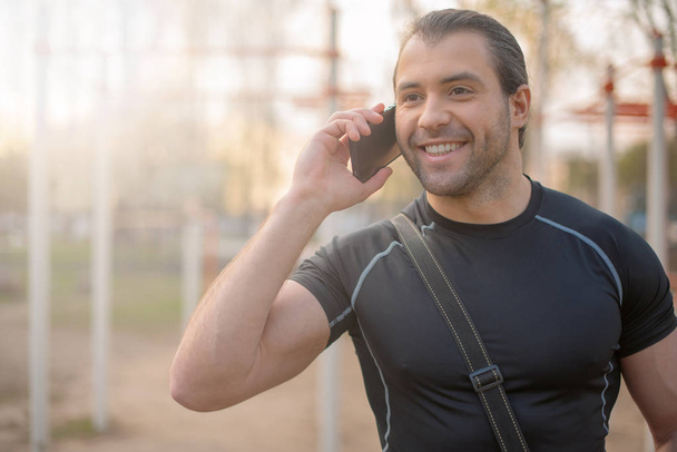 handsome male athlete, outdoors on the sports ground in the summer, smiling, talking on the phone - Foto, afbeelding