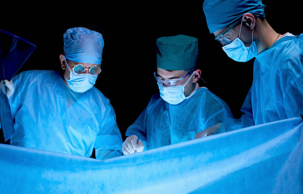 Grupo de cirujanos trabajando en quirófano tonificado en azul. Equipo médico realizando la operación - Foto, imagen