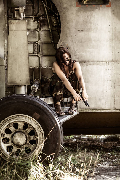 Muotokuva nuoresta tytöstä, jolla on mimeettinen sotilaspuku lähellä vanhaa hylättyä lentokonetta. Käsite sotilaallinen vahva nainen
. - Valokuva, kuva
