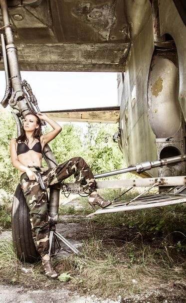 Portrait of a young girl with mimetic military dress near the old abandoned broken plane. Concept military strong woman. - Foto, imagen