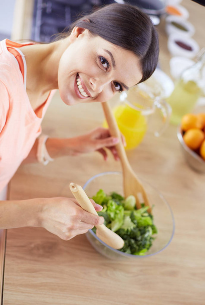 Smiling young woman mixing fresh salad in the kitchen. - 写真・画像
