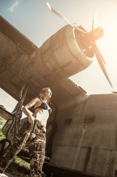 Retrato de uma jovem com vestido militar mimético perto do velho avião quebrado abandonado. Conceito militar mulher forte
. - Foto, Imagem