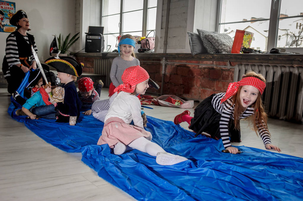 RUSSIA, YAROSLAVL - 17 FEB. 2018: happy group of children at a birthday celebration dressed in the style of pirates with an animator, contests and bubbles play games in a large room with loft style - Photo, image