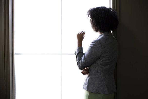 Silhouette of a black African American businesswoman thinking by the office window. She is brainstorming or planning for her startup business.  - Foto, Imagem