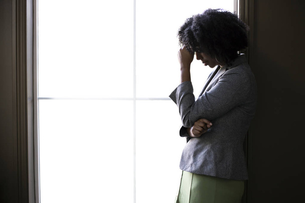 Silhouette of a stressed out black African American businesswoman looking worried and thinking about problems and failure by the office window.  She looks depressed or upset about debt or bankruptcy. - Foto, Imagem