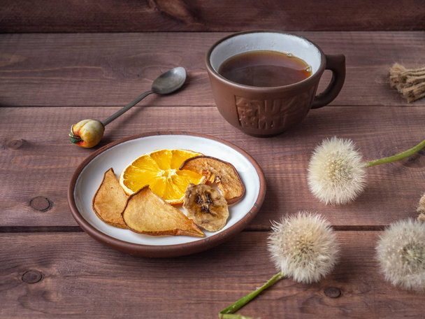 Фруктові чіпси, здорова закуска з ранковою кавою в коричневому керамічному кубку на дерев'яному сільському лотку
 - Фото, зображення