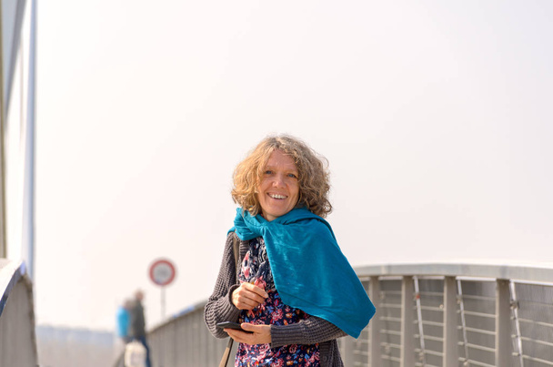 Улыбающаяся женщина в синем шарфе на мосту
 - Фото, изображение