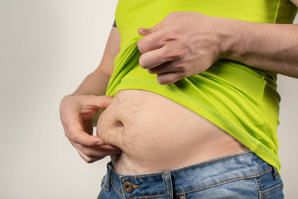 Un hombre en jeans y una camiseta con el vientre gordo sobre un fondo blanco
 - Foto, imagen