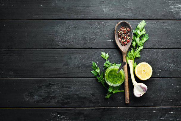 Ingredients for chimichurri sauce: fresh parsley, onion, garlic, olive oil, lemon. On a black background. Top view. free space for your text. - Foto, afbeelding
