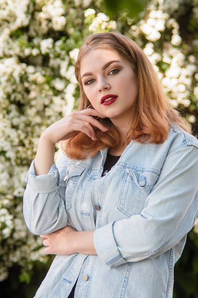A girl in a jeans jacket in the park in the background of white flowers. - Fotografie, Obrázek