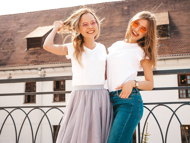 Portrait of two young beautiful blond smiling hipster girls in trendy summer white t-shirt clothes. Sexy carefree women posing on street background. Positive models having fun.Hugging - Zdjęcie, obraz