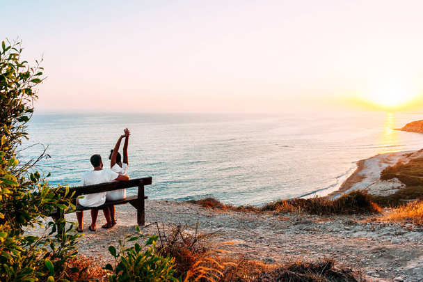 Happy couple at sunset. Man and woman at dawn. Couple sitting on a bench by the sea. Couple in love kissing by the sea. Man and woman traveling. Honeymoon trip. Sunset on sea. Dawn by the sea - Foto, immagini
