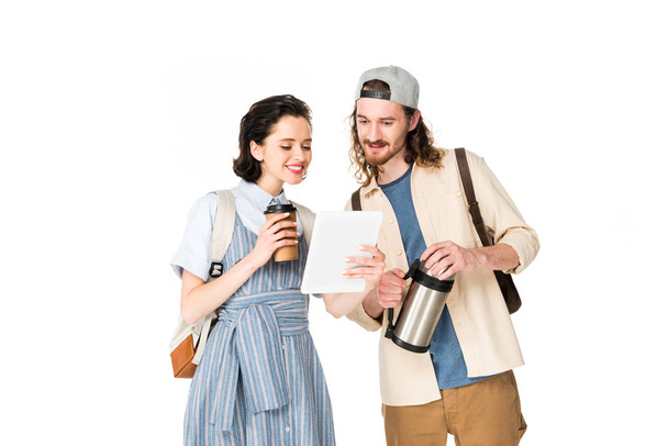 νεαρός άνδρας και κορίτσι κοιτάζοντας τη συσκευή, κρατώντας χάρτινο φλιτζάνι καφέ και θερμός απομονώνονται σε λευκό - Φωτογραφία, εικόνα