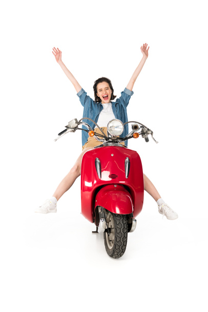 volledige lengte weergave van meisje zittend op rode scooter met haar handen in de lucht isoalted op wit  - Foto, afbeelding