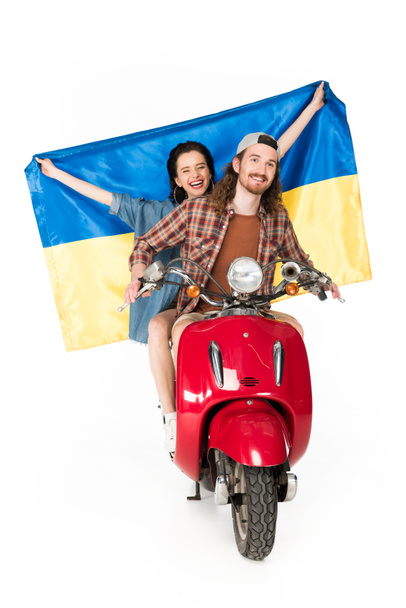 vista completa de la muchacha sentada en scooter rojo y sosteniendo la bandera de Ukranian y el hombre joven mirando hacia adelante aislado en blanco
 - Foto, Imagen