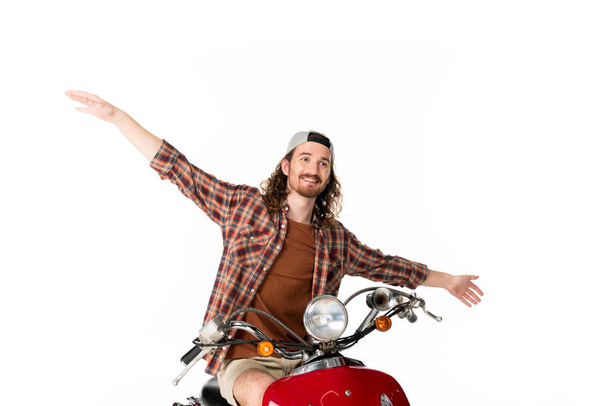young handsome man riding on red scooter put hands in air isolated on white - Фото, изображение