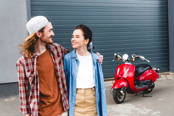молодий чоловік і дівчина стоять біля червоного скутера і обіймаються
 - Фото, зображення