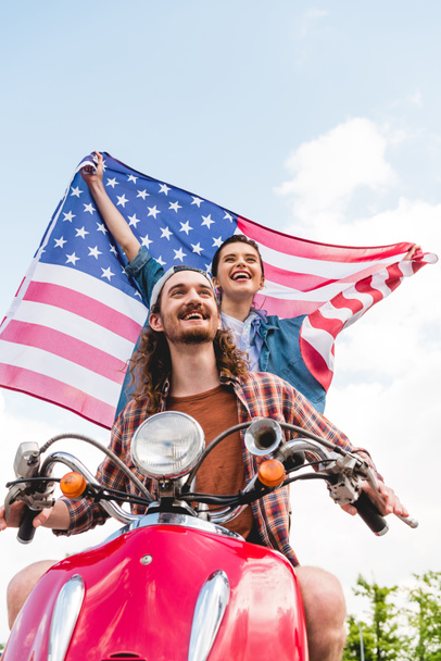 low angle view of beautiful girl standing behind young man and holding flag on sky background - Photo, Image