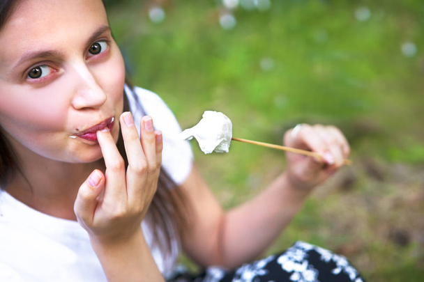 kaunis nuori nainen syö vaahtokarkkeja keitetty nuotiolla luonnossa
 - Valokuva, kuva