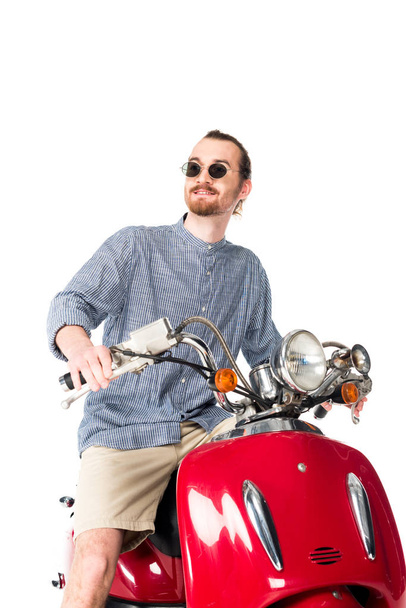 low angle view of handsome stylish young man sitting on red scooter isolated on white - Фото, зображення