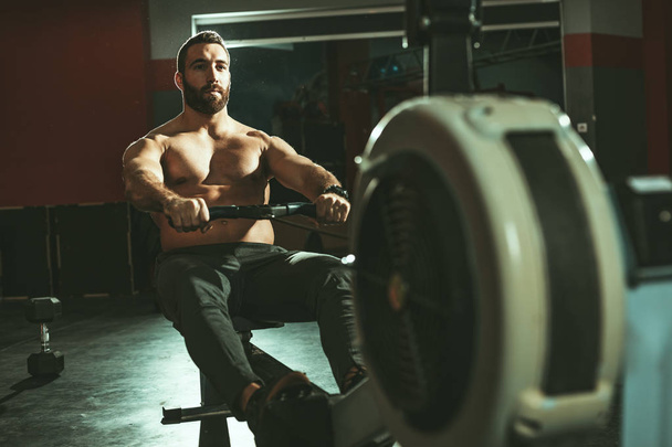 Muscular man pulling rowing machine in gym - Foto, imagen
