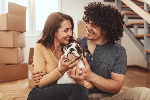 young couple playing with little bulldog puppy in new home - Photo, Image