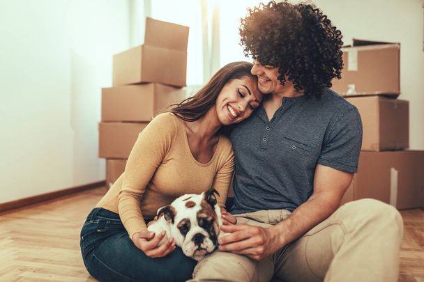 Close view portrait of cheerful couple playing with bulldog puppy in new apartment  - Photo, Image