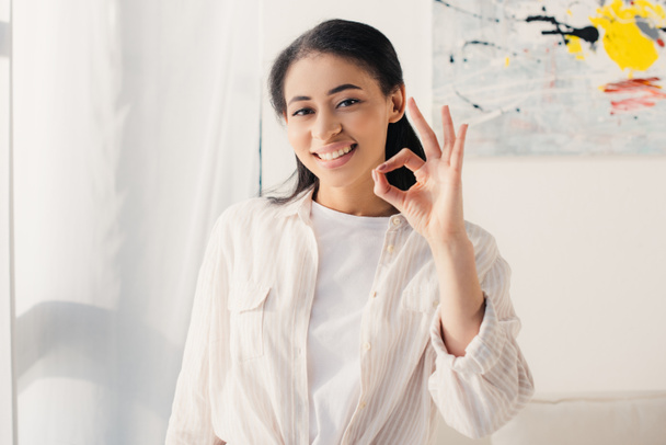 cheerful latin woman showing ok gesture while smiling at camera - Fotoğraf, Görsel