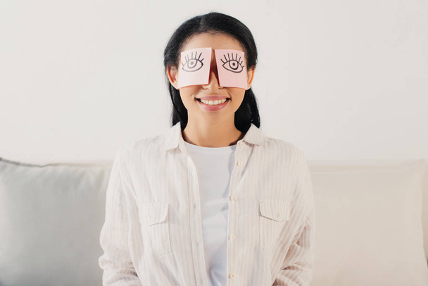 smiling latin woman with eyes covered with sticky notes with drawn eyes - Photo, Image