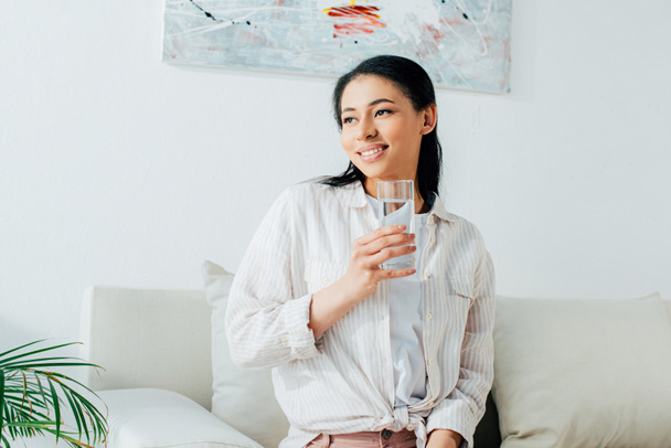 beautiful lating woman smiling and looking away while holding glass of water - Fotografie, Obrázek