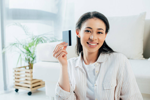 alegre latina sosteniendo tarjeta de crédito mientras sonríe a la cámara
 - Foto, Imagen