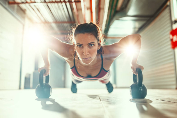 Jovem mulher muscular fazendo exercício com kettlebells em treinamento duro
 - Foto, Imagem